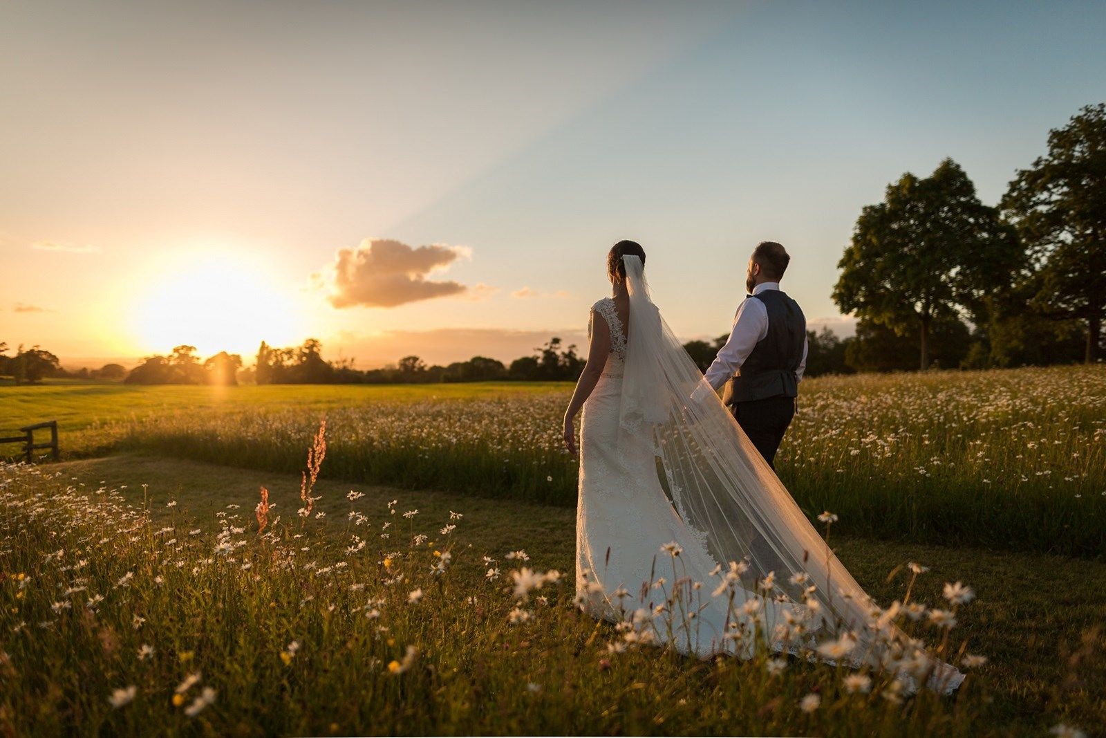 a bride and groom are walking through a field of flowers at sunset .
