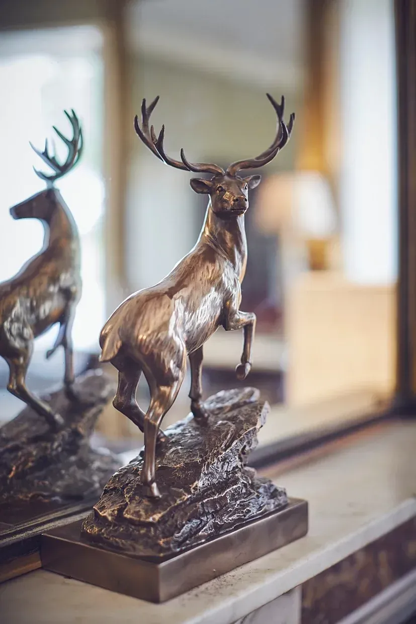 a bronze statue of a deer standing on a rock in front of a mirror .