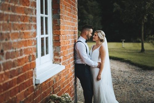 a bride and groom are leaning against a brick wall .