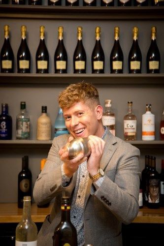 a man in a suit is shaking a bottle of wine in a bar .