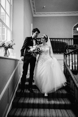 a black and white photo of a bride and groom walking down stairs .