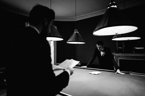 a man is reading a book while standing next to a pool table .