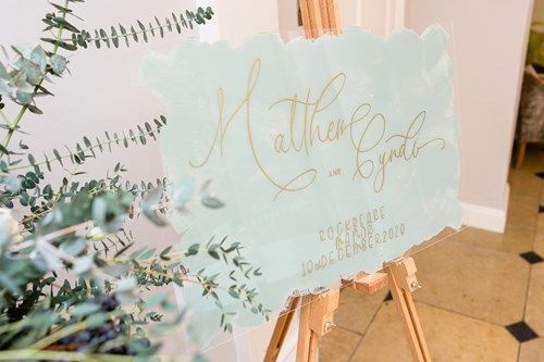 a sign on a wooden easel with flowers in the background .