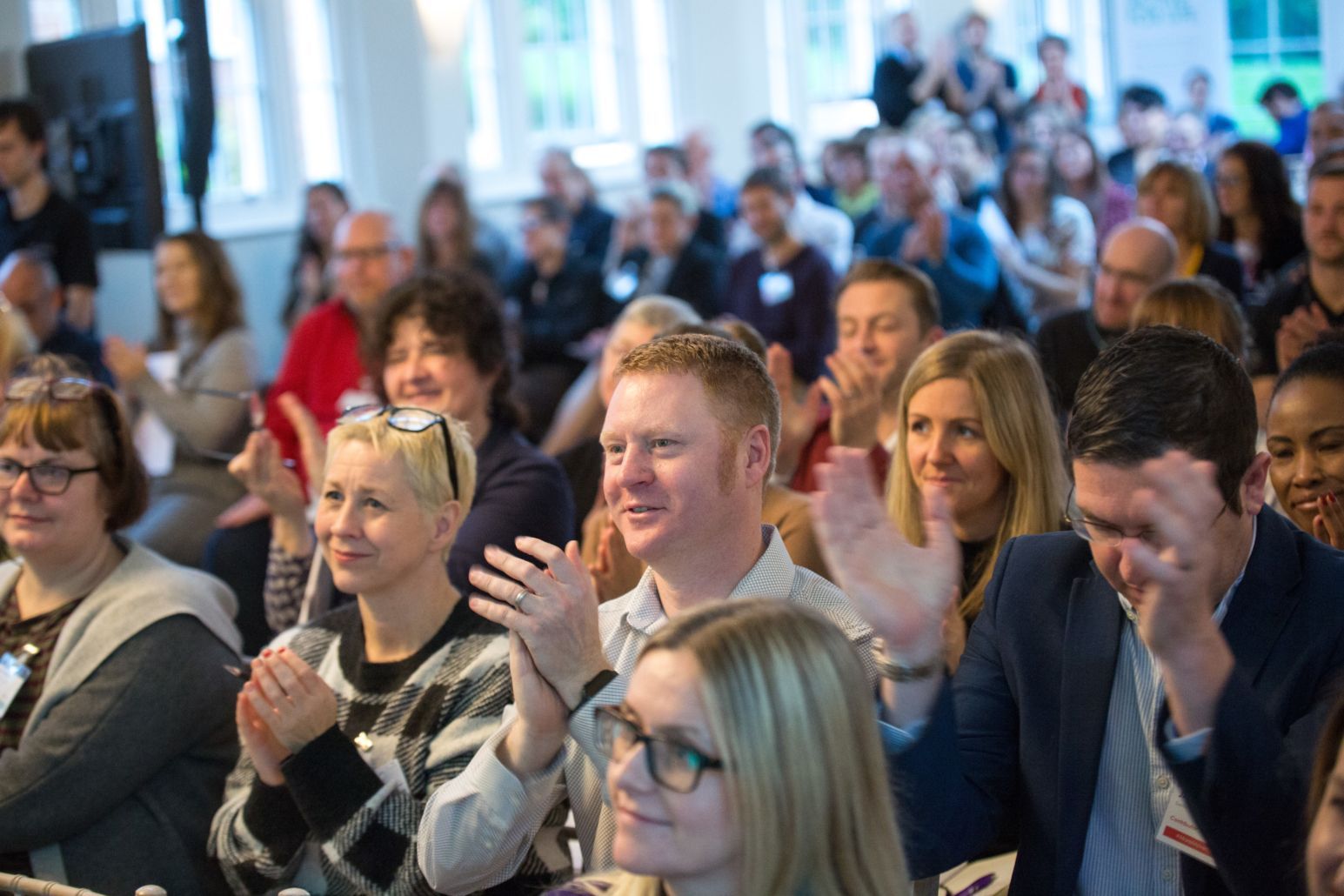 a large group of people are sitting in a room applauding .