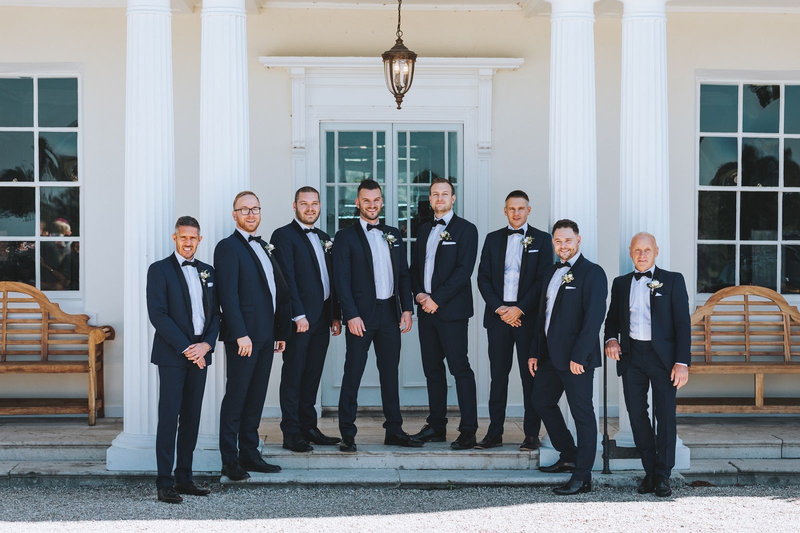 a group of men in tuxedos are standing in front of a building .