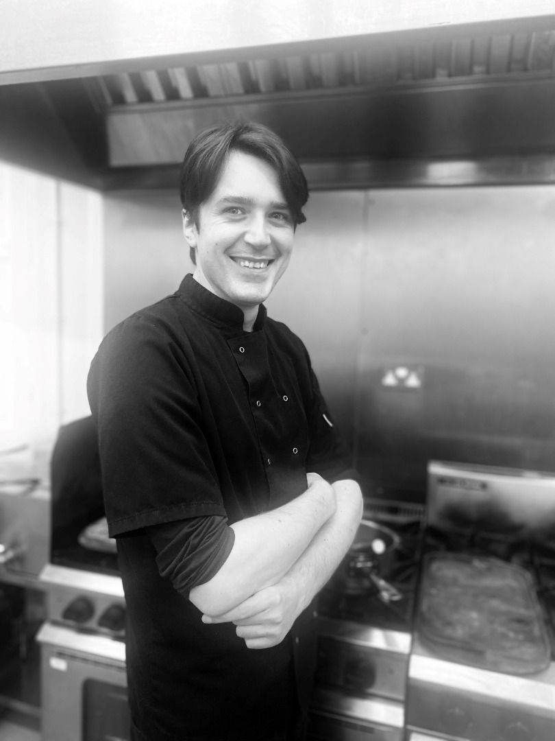 a man is standing in a kitchen with his arms crossed and smiling .