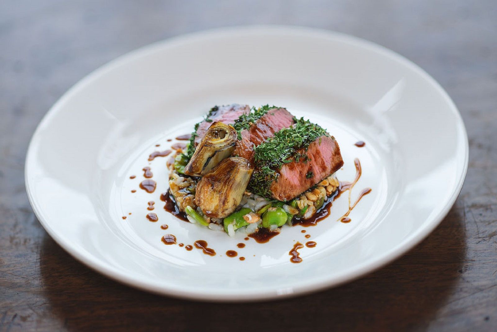 a white plate topped with meat and vegetables on a wooden table .