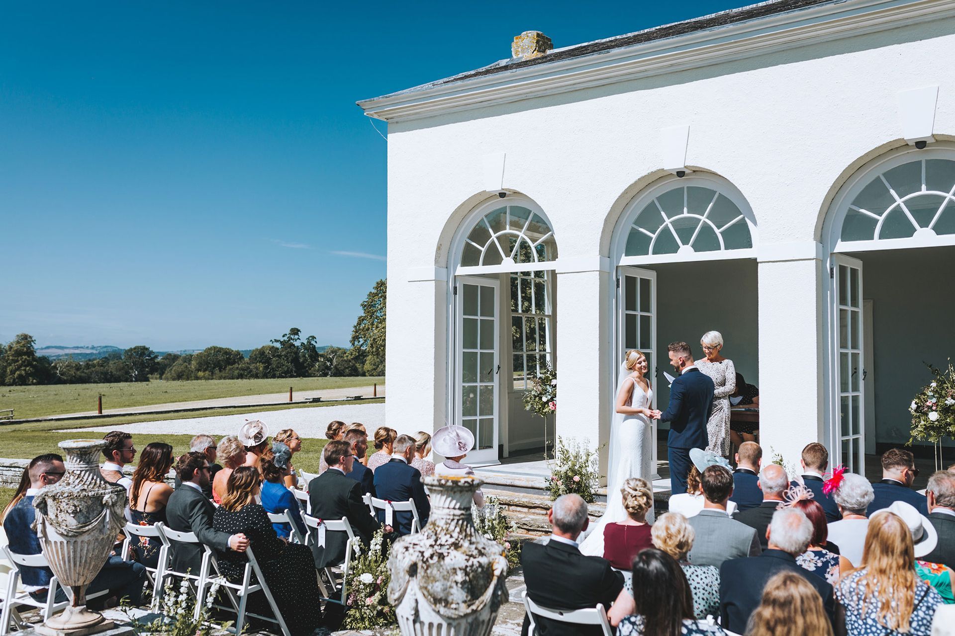 a group of people are sitting in front of a white building watching a wedding ceremony .
