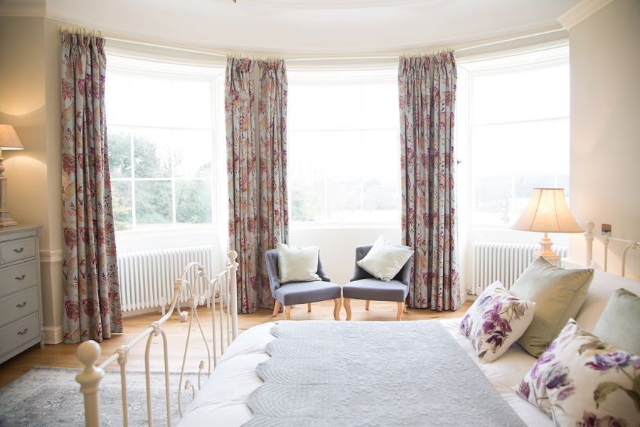 a bedroom with a bed , chairs , curtains and a large window .