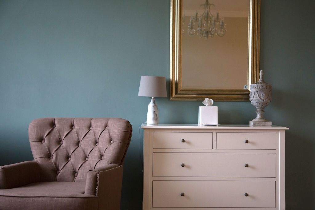 a living room with a chair , dresser , lamp and mirror .