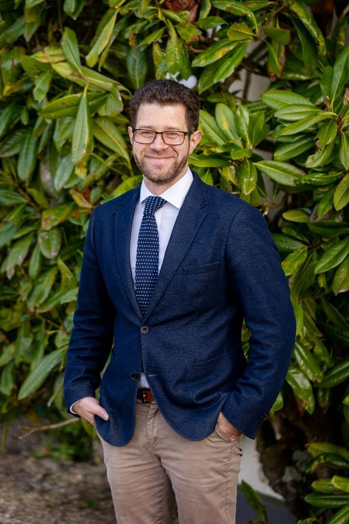 a man in a suit and tie is standing in front of a bush .