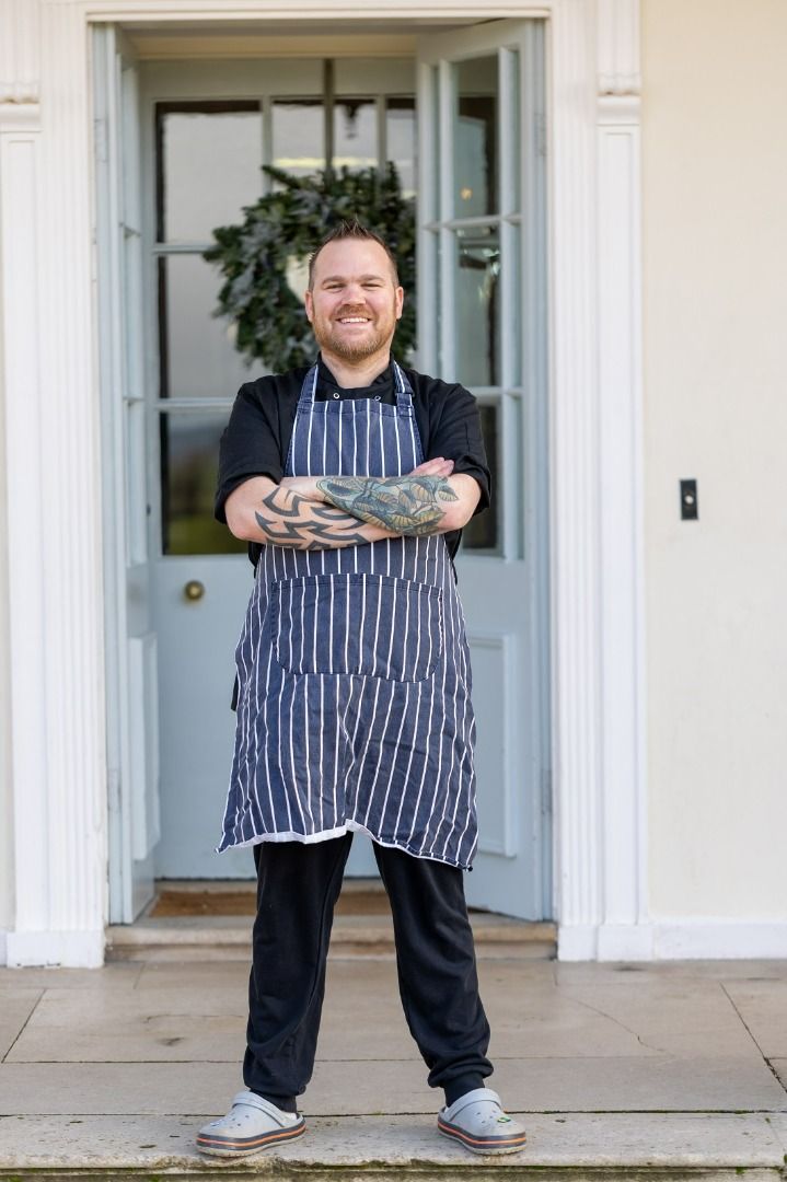 a man in an apron is standing in front of a door with his arms crossed .