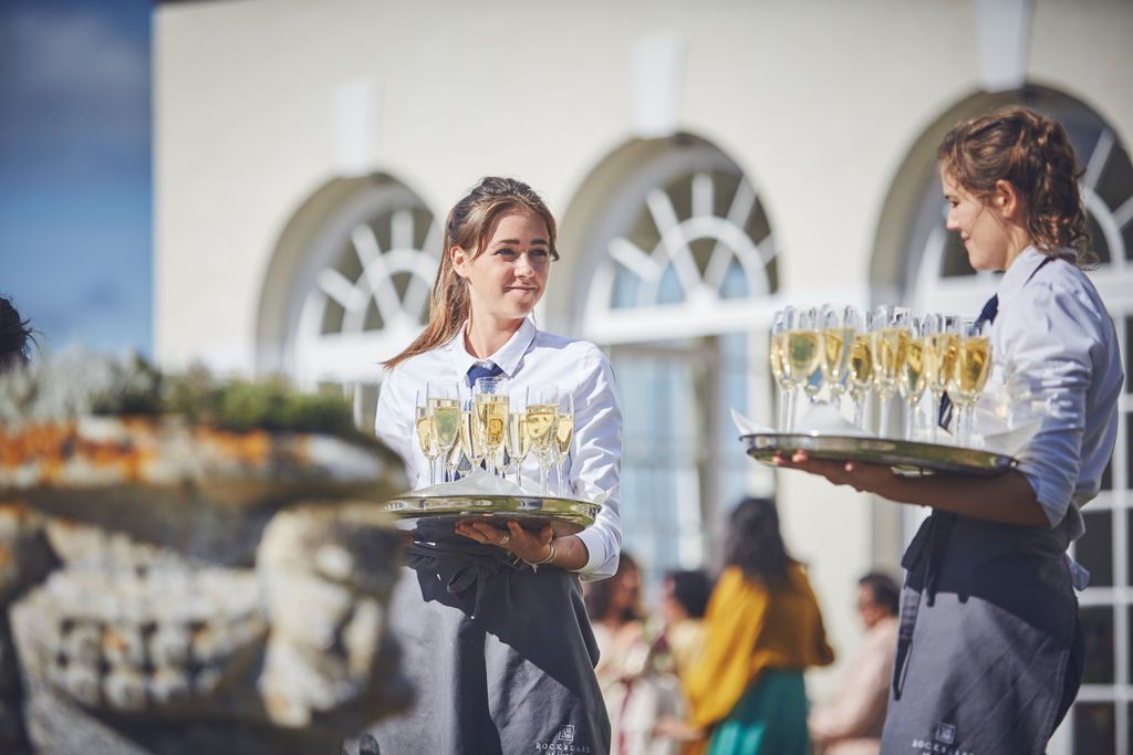 two women are carrying trays of champagne glasses .