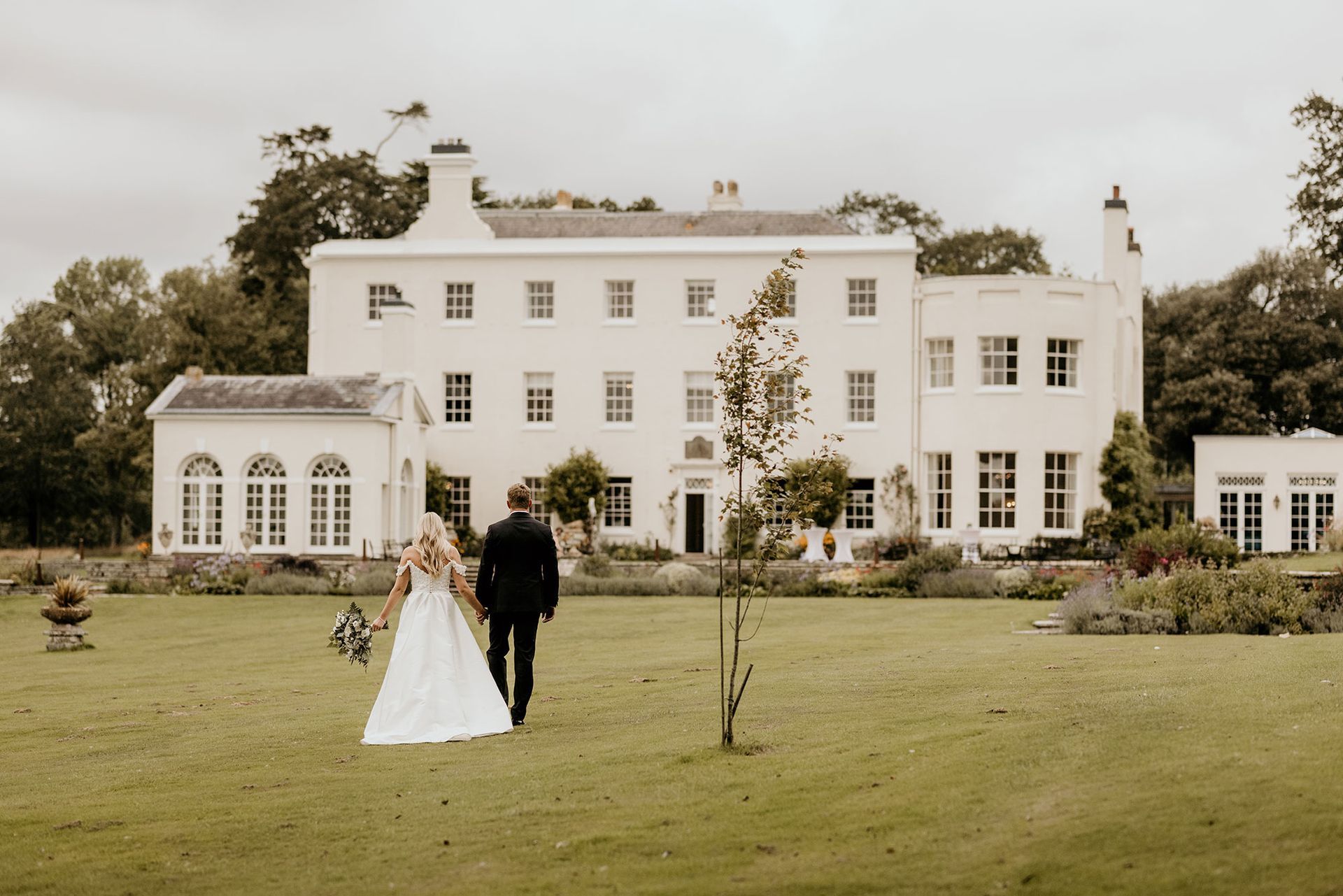 a bride and groom are walking in front of a large white building. wedding venue in Exeter Devon.