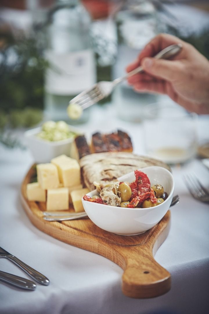 a person is holding a fork over a bowl of food on a wooden cutting board .