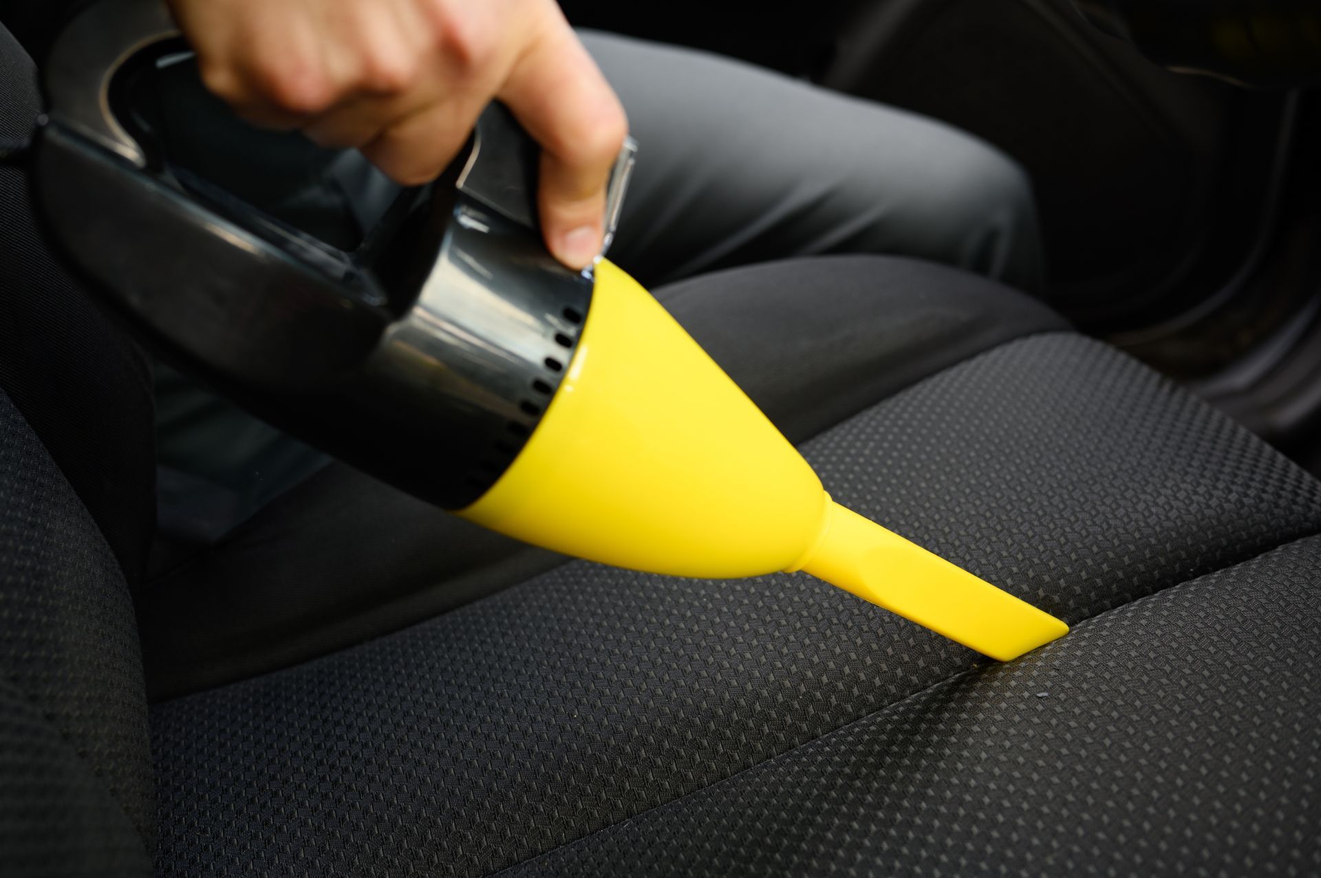 A person is using a yellow vacuum cleaner to clean a car seat