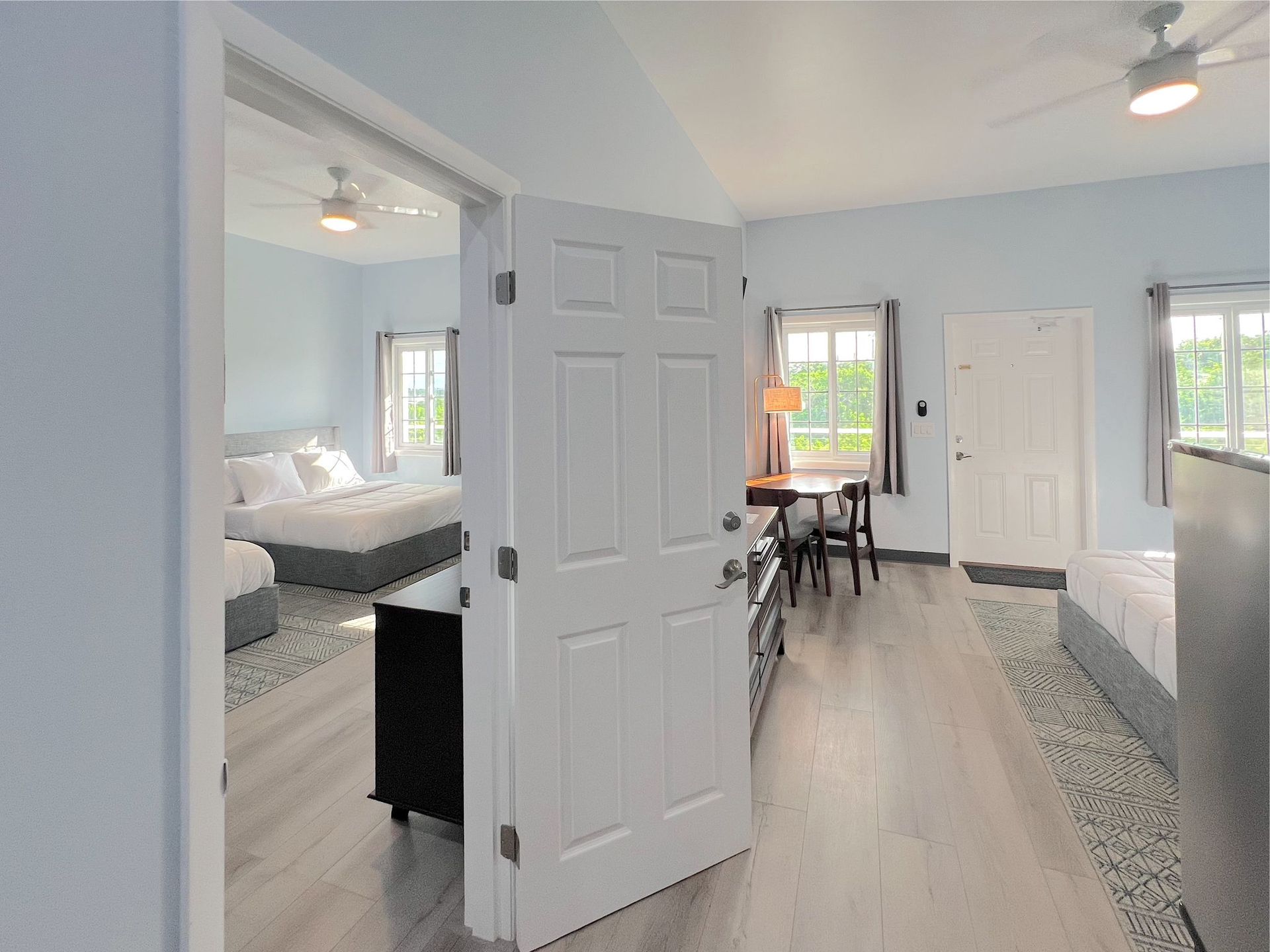 Interior view of a light blue-walled room, with open doors leading to other rooms, beds, and a table.