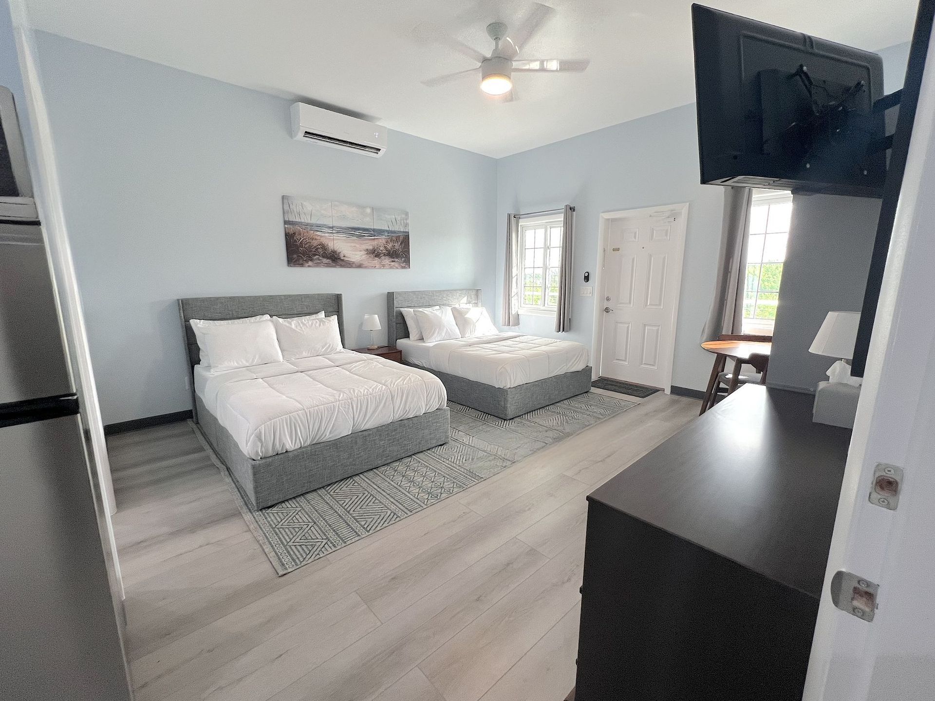 Bedroom with two gray beds, blue walls, a TV, and a dresser.