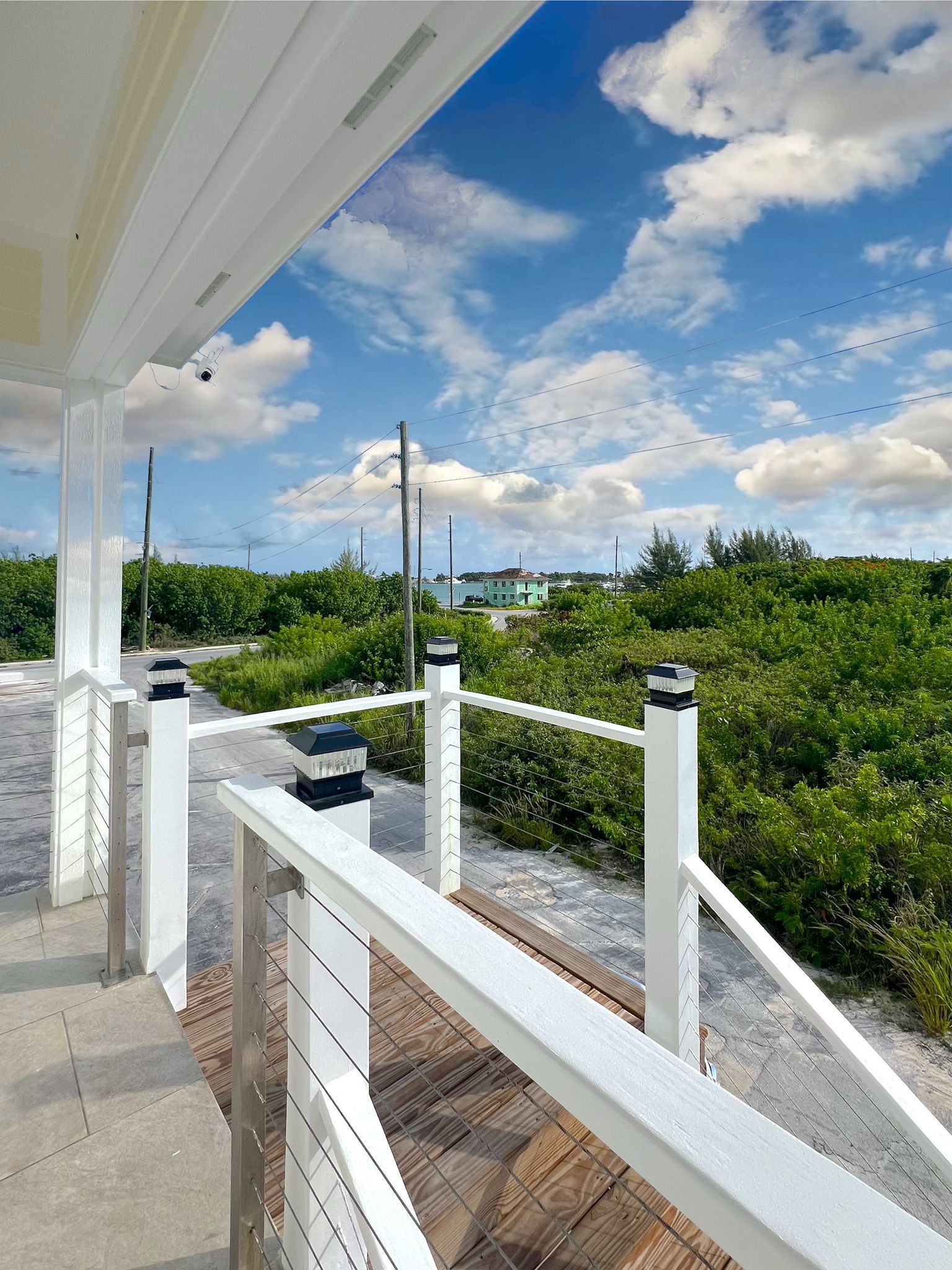 White railing overlooks lush green vegetation and a blue sky with clouds.