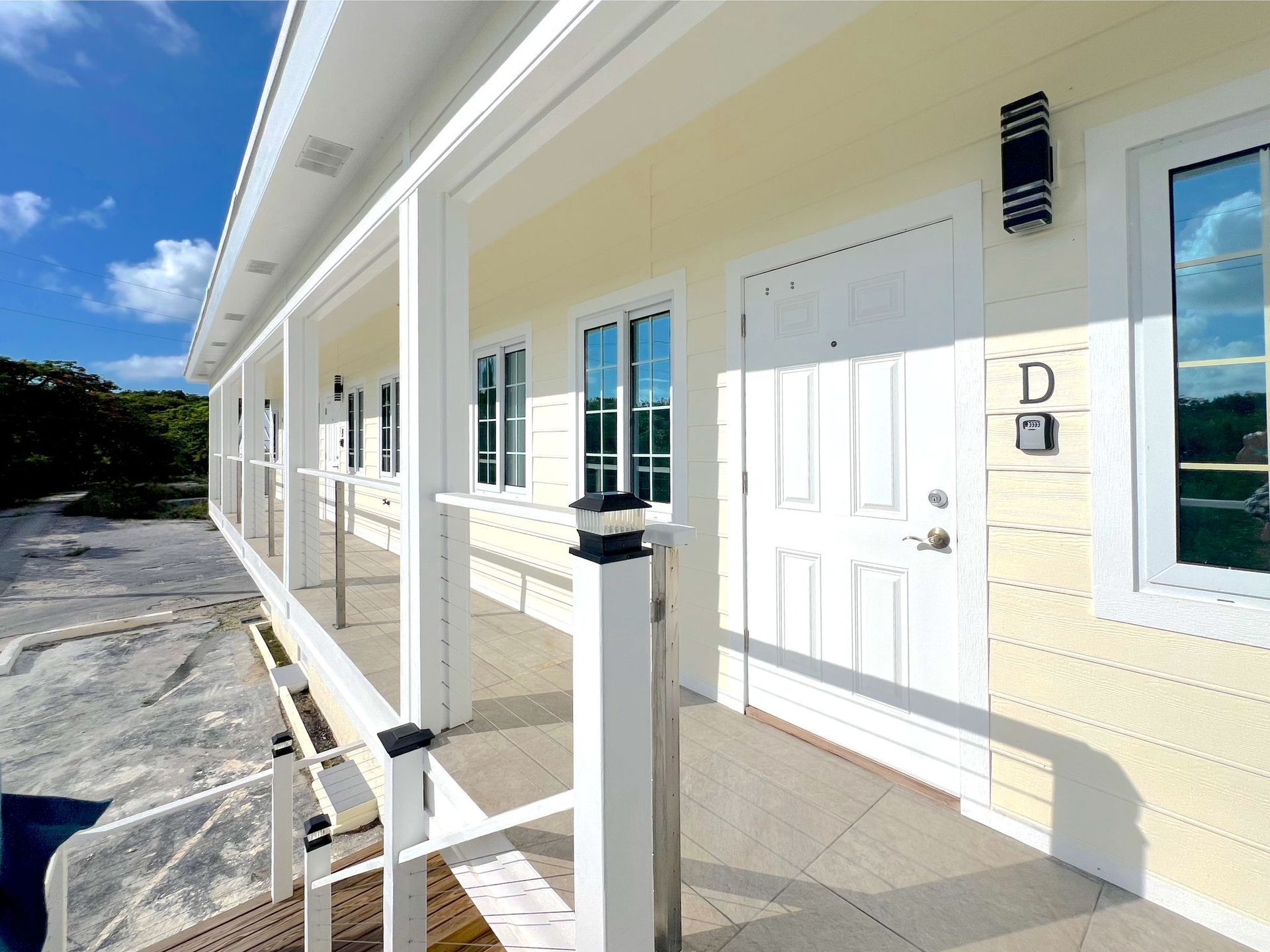 Exterior of a light yellow building with a covered porch and white trim. Blue sky and some trees visible.
