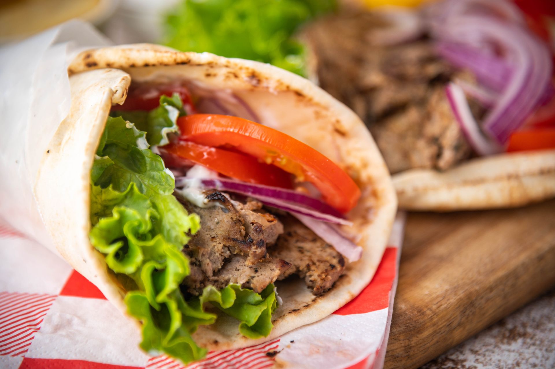 Gyros sandwich with lettuce, tomato, onions, and meat wrapped in pita.