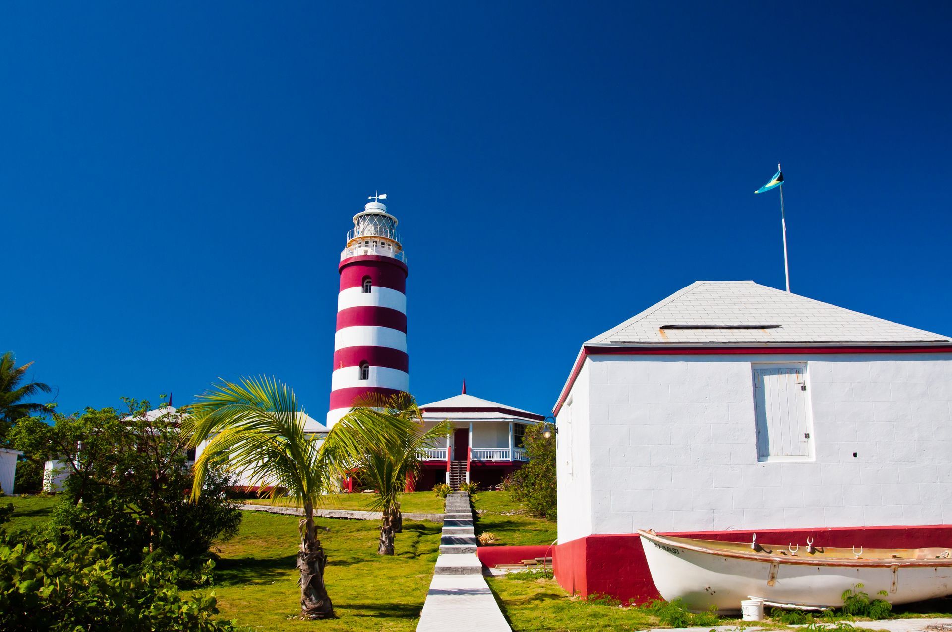 Striped red and white lighthouse and white building under blue sky.