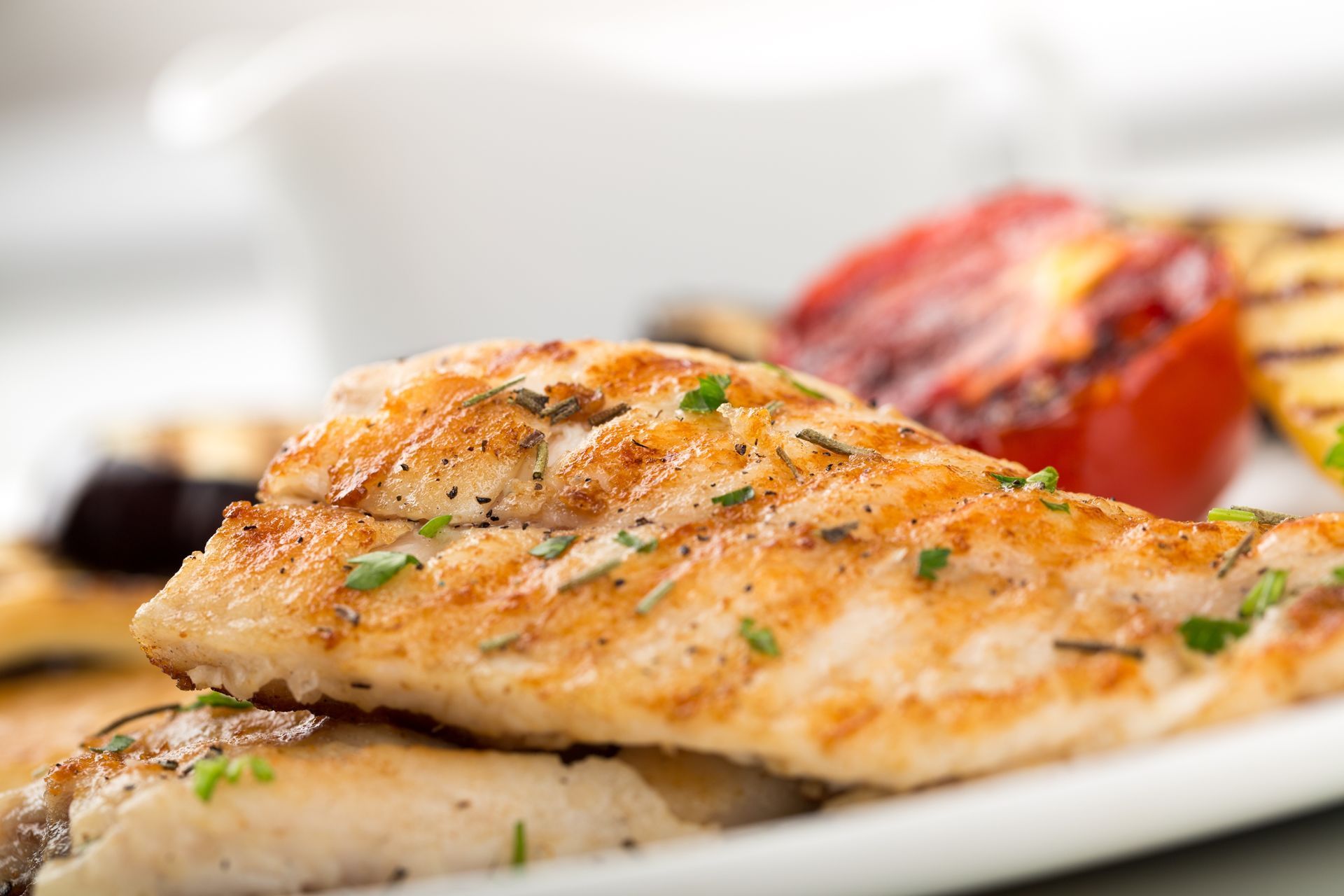 Pan-seared fish fillet with grilled tomato and zucchini on a white plate.
