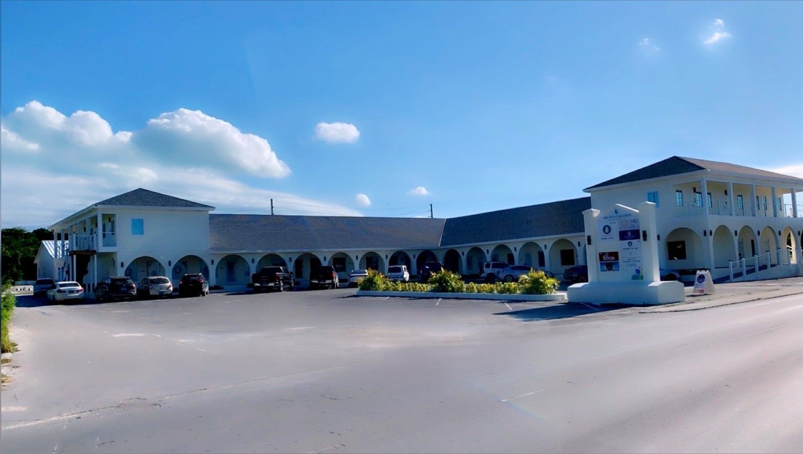 White railing and posts on a deck overlooking green bushes, with a blue sky and clouds overhead.