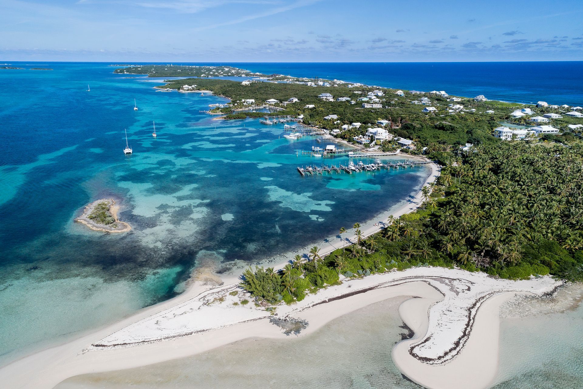Aerial view of a tropical island with turquoise water, white sand, lush green vegetation, and scattered buildings.