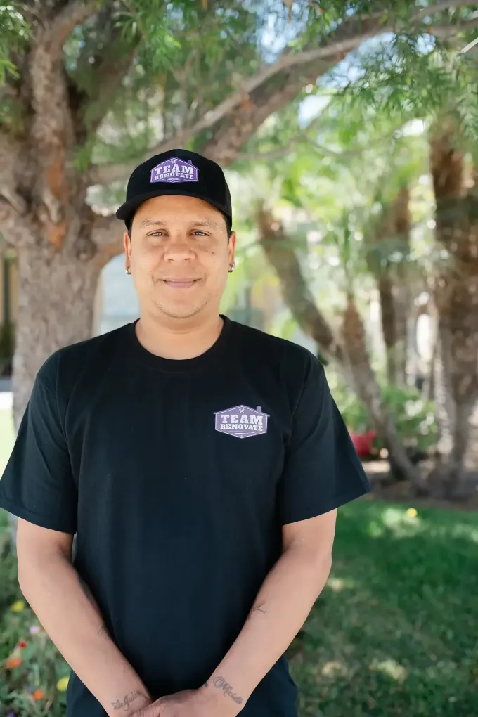 A man wearing a hat and a black t-shirt is standing in front of a tree. Miguel team  at Team Renovate in San Diego , Home remodeler