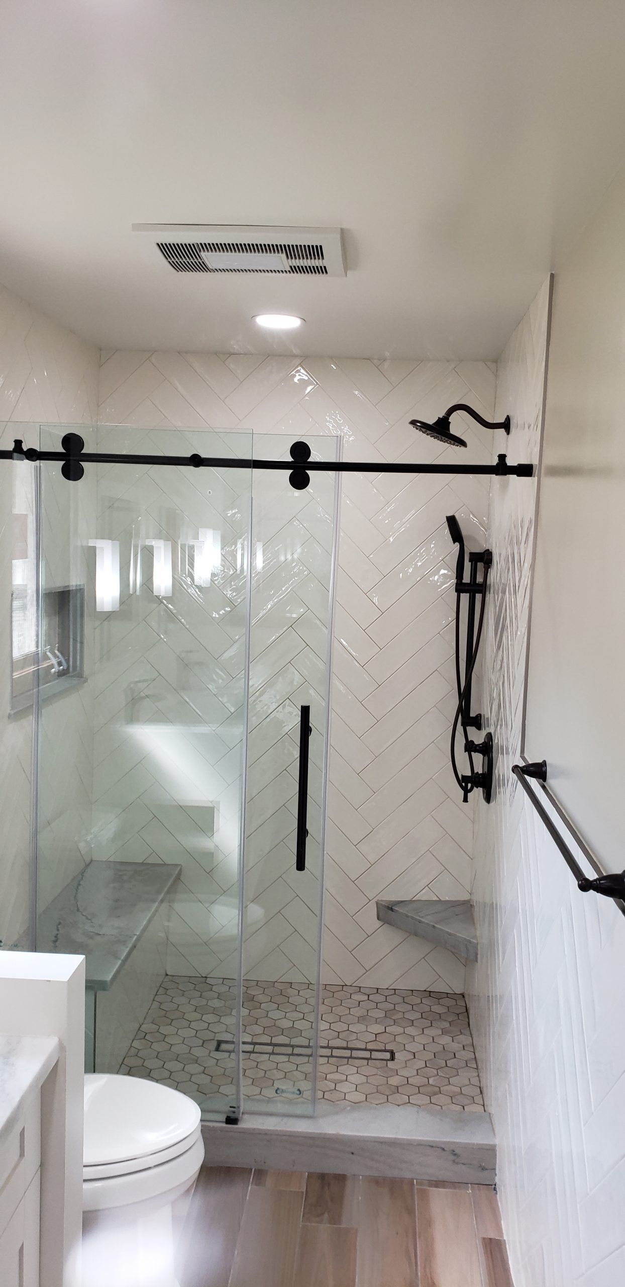 A bathroom with a toilet and a shower with a sliding glass door from a Bathroom remodel in San Diego CA by Team  Renovate