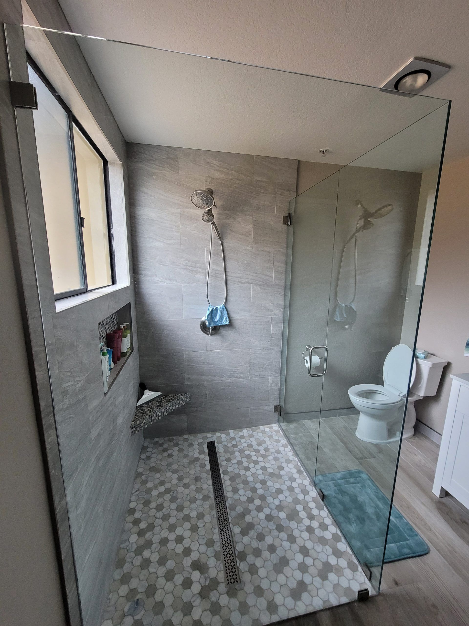 A bathroom with a walk in shower, toilet and window.