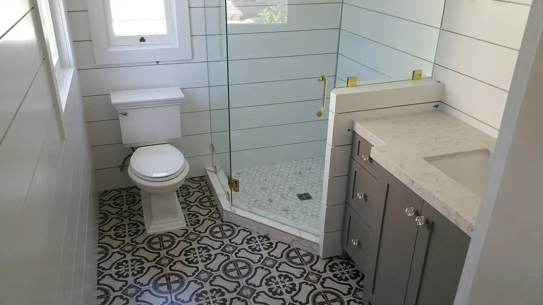 A bathroom with a toilet , sink and shower. Bathroom remodel with gold accents in Point Loma