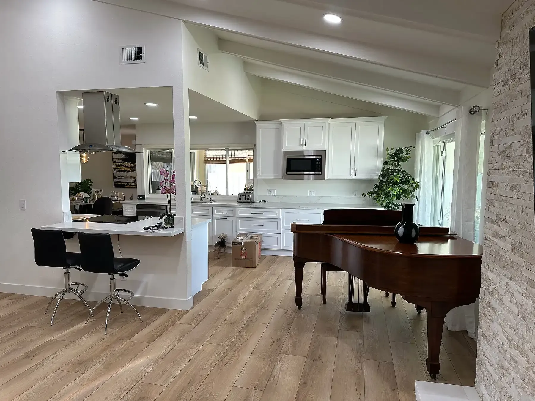 A living room with a piano and a kitchen in the background.