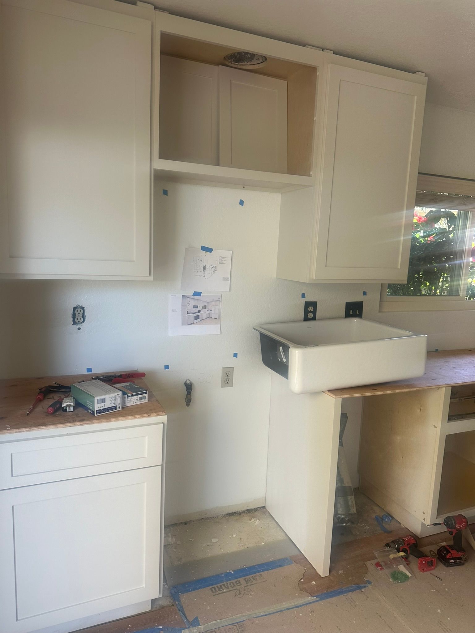 Team Renovate - Kitchen cabinets being installed, with unfinished walls and countertop, and a sink installed.