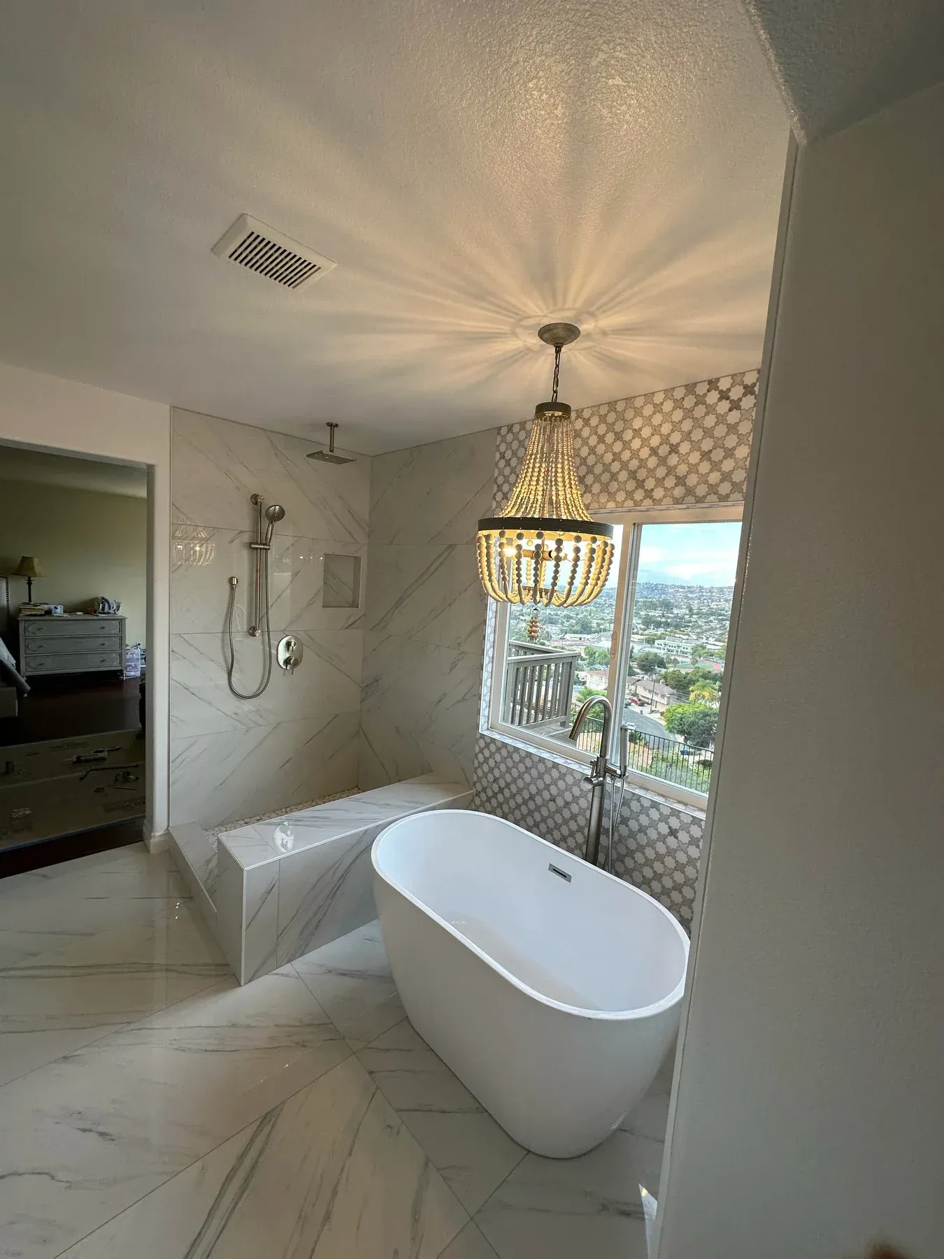A bathroom with a bathtub , shower , and chandelier from a Bathroom remodel in San Diego CA by Team  Renovate