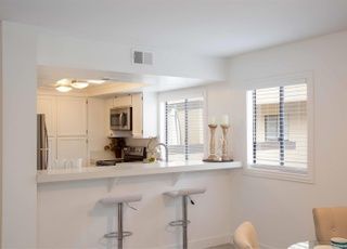A kitchen with a counter , stools , a refrigerator and a microwave.