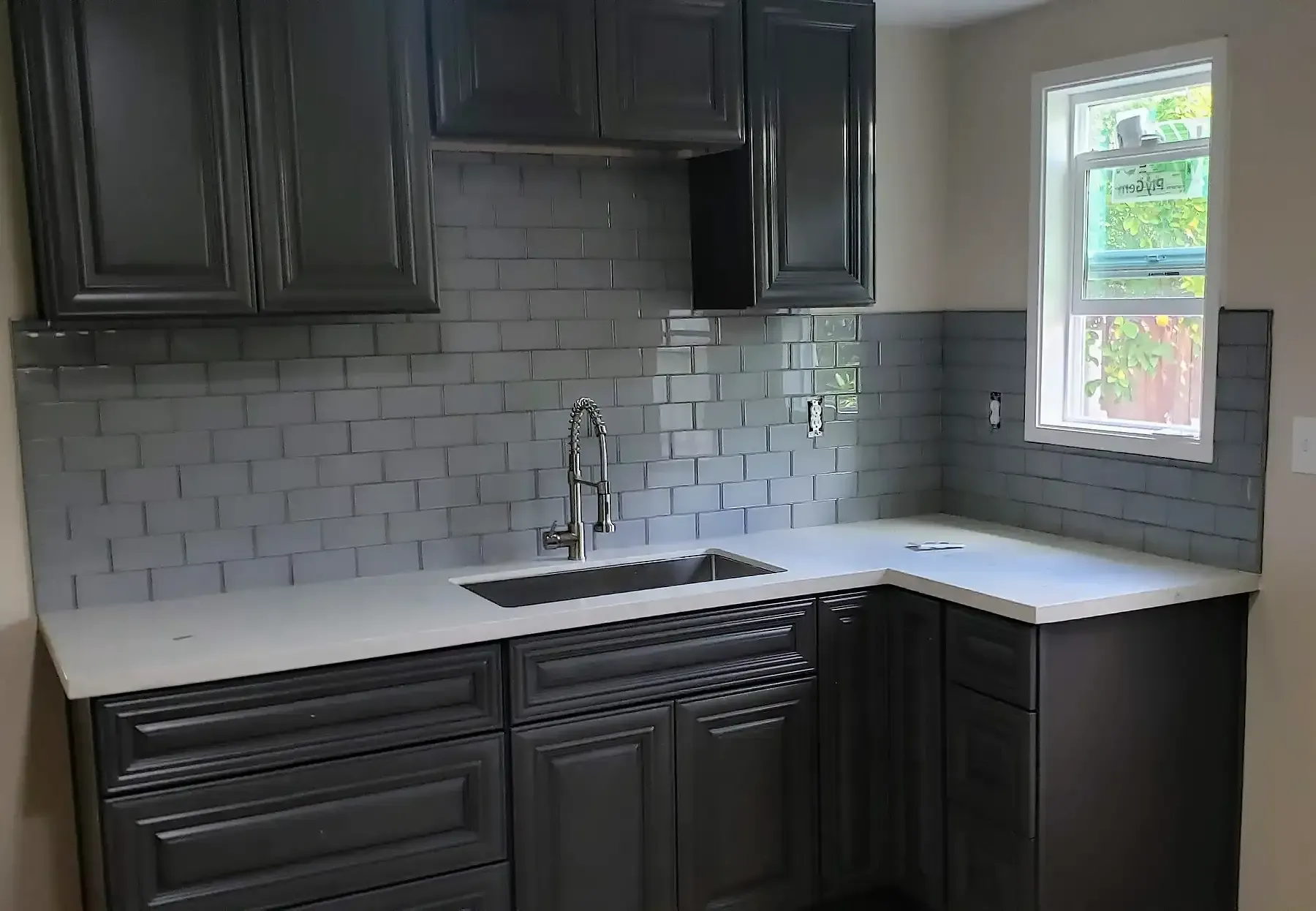A laundry room with gray cabinets , a sink , and a window.