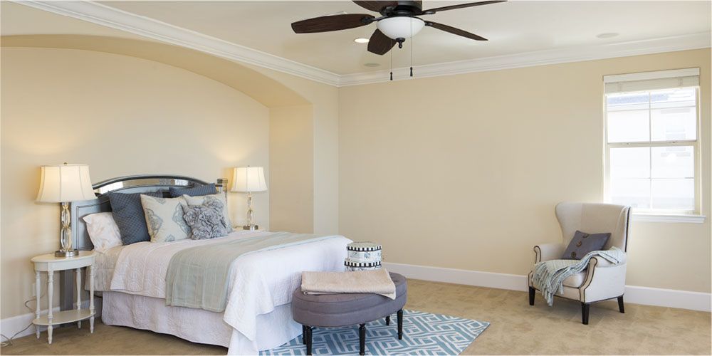 A bedroom with a bed , chair and ceiling fan.