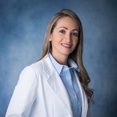 A woman in a white lab coat and blue shirt is smiling for the camera.