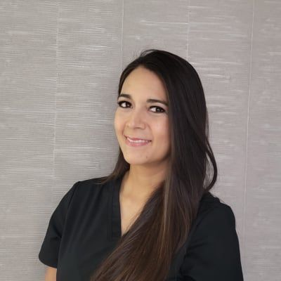 The woman is wearing a black scrub top and smiling for the camera.