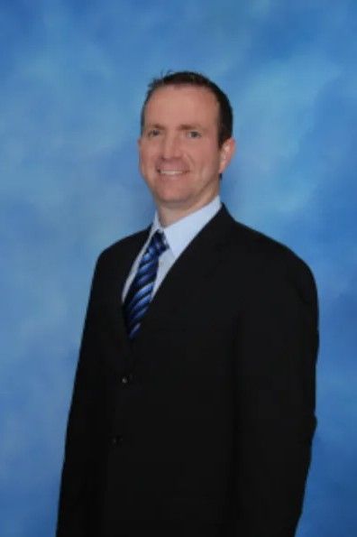 A man in a suit and tie stands in front of a blue background