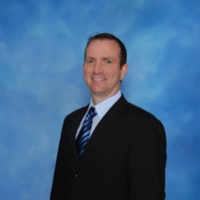 A man in a suit and tie stands in front of a blue background