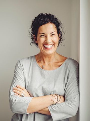 A woman is leaning against a wall with her arms crossed and smiling.