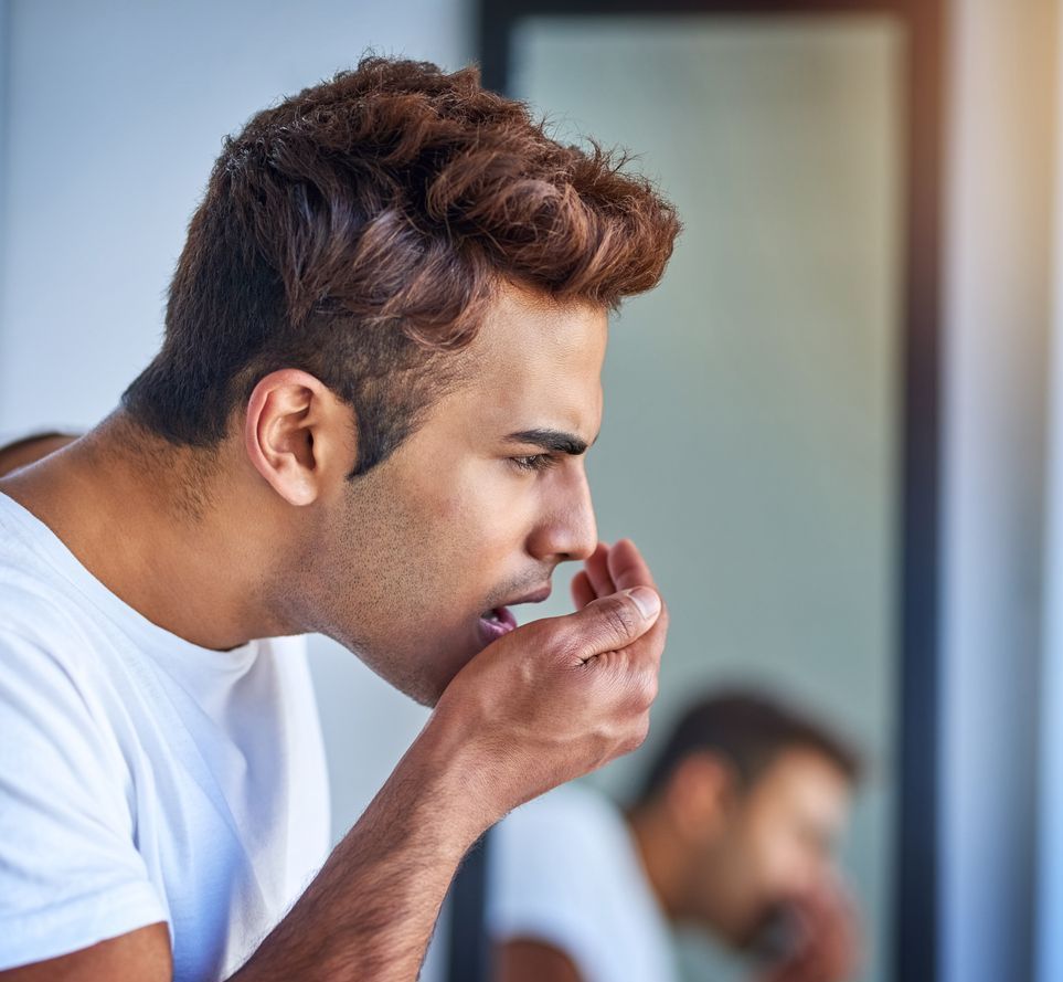 A man is covering his mouth with his hand in front of a mirror.