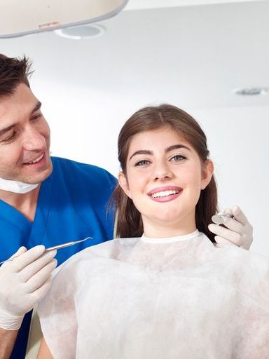 A woman is sitting in a dental chair while a dentist examines her teeth