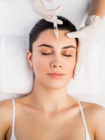 A woman is getting a botox injection in her forehead.