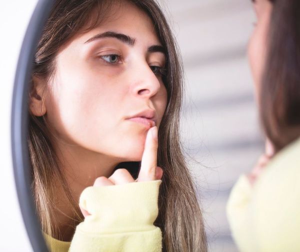 A woman is looking at herself in a mirror with her finger on her lips.