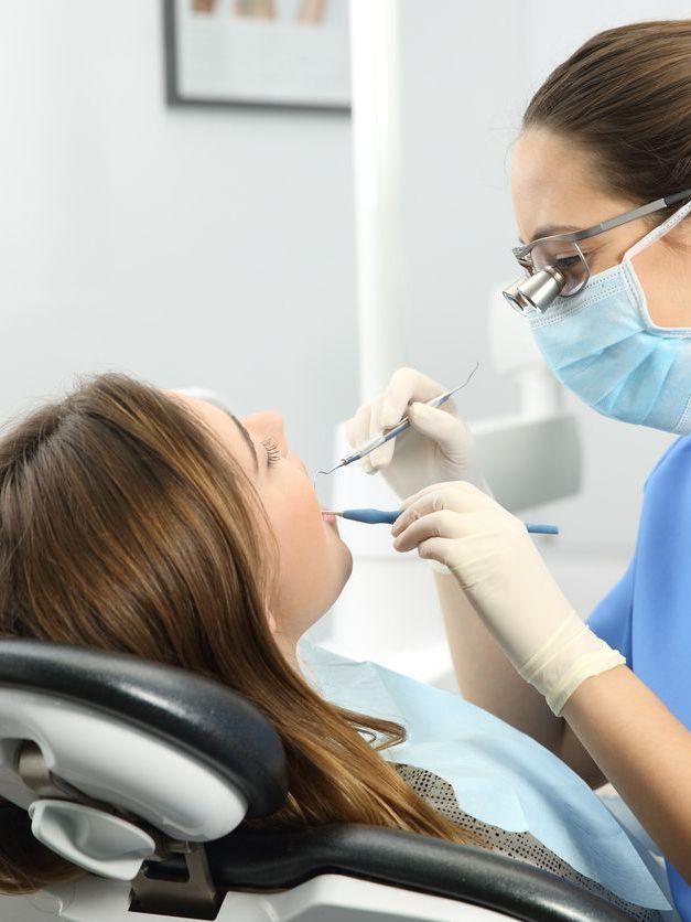 A woman is sitting in a dental chair getting her teeth examined by a dentist.