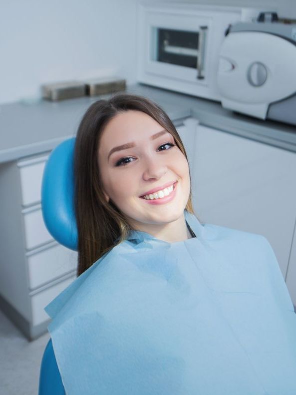 A woman is smiling while sitting in a dental chair.